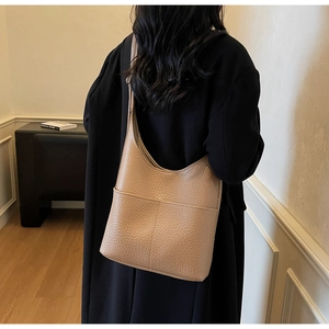 Close-up of beige leather tote bag with lychee texture and shoulder strap on model