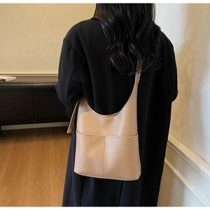 Beige pebble leather hobo bag with front pockets shown on shoulder in a lifestyle setting