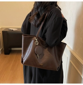 Close-up of deep brown leather tote bag with gold logo text and round coin purse charm