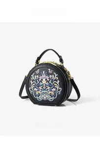 Detail of colorful floral embroidery on a black circular crossbody bag with dual zippers
