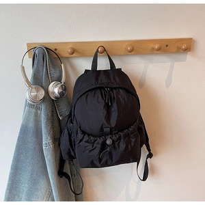 Detail of black nylon backpack with quilted fabric and drawstring front pocket in a lifestyle setting