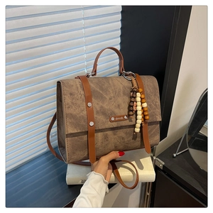 Détail d'un sac messager marron vintage avec sangles décoratives et breloque perlée