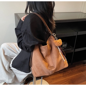 Braune Wildleder-Tasche mit Bärenanhänger und Band auf der Schulter eines Models
