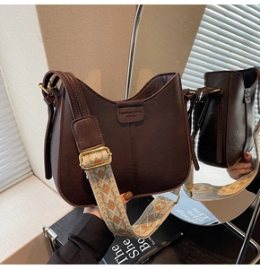Détail d'un sac demi-lune marron foncé avec une bandoulière tissée bohème colorée