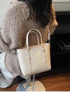 Beige woven leather bucket bag with top handles and adjustable strap on a female model