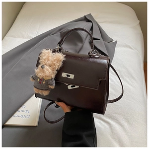 Detailed view of dark brown glossy leather handbag with silver turn-lock and teddy bear charm