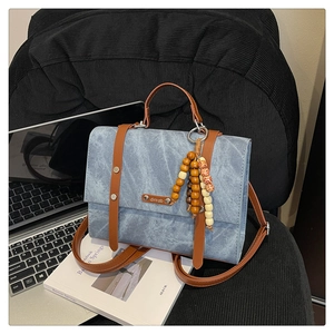 Détail du sac à main en denim bleu avec lanières en cuir marron et breloque en bois