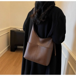 Detail of dark brown pebble leather hobo bag on a model wearing a black coat