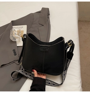 Détail du sac seau noir en cuir avec bandoulière géométrique et boucles dorées