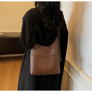 Detailed shot of brown pebbled leather bucket bag with large pocket worn by model