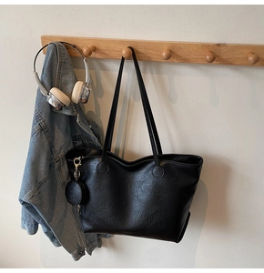 Close-up of black textured tote bag with small detachable pouch on a wooden hook