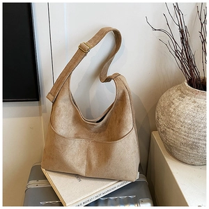 Dettaglio della borsa a mezzaluna in camoscio marrone su una valigia, stile hobo minimal