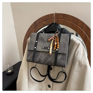 Détail d'un sac à dos vintage gris avec sangles en cuir et breloque décorative en perles de bois