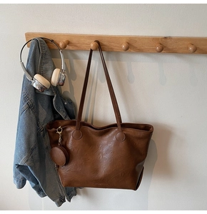 Detailed view of large brown tote bag with mini round pouch hanging on a coat rack