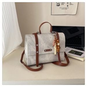 Détail du sac gris clair texturé avec lanières brunes et pendentif artistique en perles