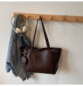 Detail view of large dark brown leather tote bag with round coin purse hanging on wood hook