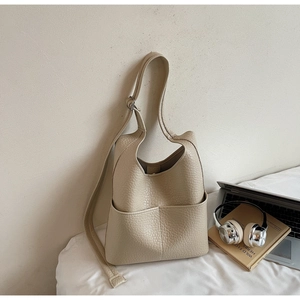 Detail of cream white pebbled leather bucket bag on a bed with lifestyle accessories