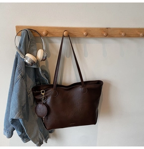 Detail of dark brown tote bag with small matching purse hanging on a wooden hook