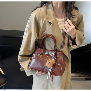 Brown leather handbag detail featuring metal buckle, zip pocket, and bear charm