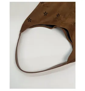 Detail of dark brown suede tote featuring hollow flower patterns and reinforced handle