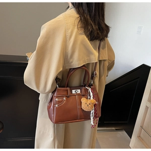 Detail view of a vintage dark brown leather handbag with metal rivets and a cute bear charm