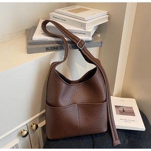 Close-up of brown litchi pattern leather bucket bag featuring dual front pockets and strap