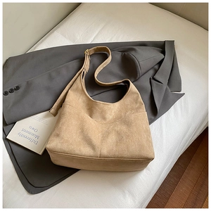 Dettaglio della borsa hobo in pelle scamosciata kaki su un letto bianco con decori