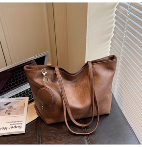 Detail of caramel brown faux leather tote bag with shoulder strap and round coin purse charm