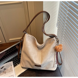 Detail der beigen Wildledertasche mit braunen Griffen und niedlichem Bärenanhänger