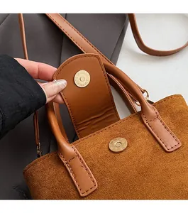 Detail of the magnetic buckle closure on a brown suede bucket bag with leather handle