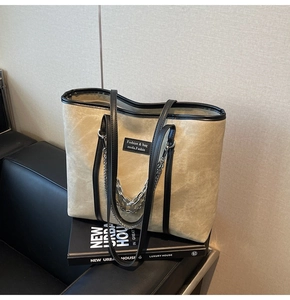 Gros plan d'un sac cabas kaki avec bandoulière en cuir, chaîne et écusson sur un canapé