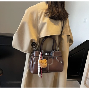 Detail of dark brown faux leather handbag with contrast stitching and teddy bear charm