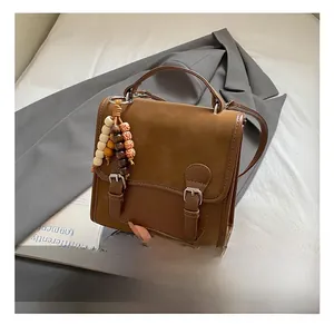 Detail view of a vintage brown leather handbag with a colorful wooden bead charm decoration