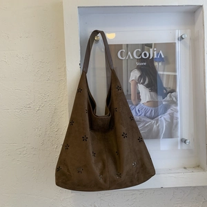 Detail of laser-cut flower patterns on a dark brown suede hobo tote bag with a wide strap
