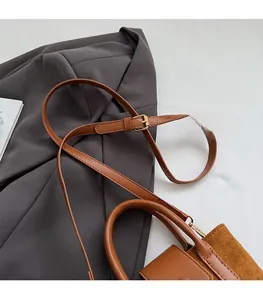Detail of adjustable leather strap and golden metal buckle on a brown suede bucket bag