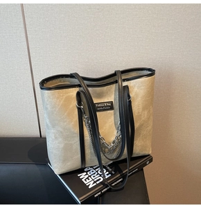 Détail du sac cabas gris-vert avec chaînes argentées et finitions en cuir noir sur un canapé
