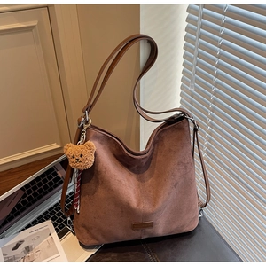 Detail einer großen braunen Wildleder-Hobo-Tasche mit vertikaler Naht und Bärenanhänger