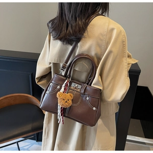 Back view of brown leather handbag with contrast stitching and teddy bear charm accessory