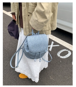 Detail of light blue textured denim backpack with drawstring and flap closure