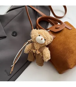 Detail of a brown plush bear keychain charm attached to a stylish bucket handbag handle