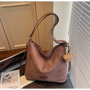 Detail einer braunen Wildleder-Hobo-Tasche mit Plüschbären-Anhänger und Leder-Logo
