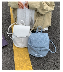Detail of white leather and blue denim drawstring backpacks with fluffy pompom accents