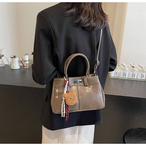 Detailed side view of brown leather handbag with contrast stitching and teddy bear charm
