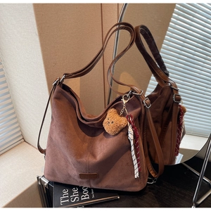 Detail einer großen braunen Wildleder-Tote-Bag mit Plüschbär-Anhänger und Web-Accessoire