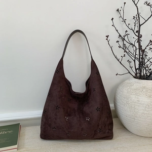 Detail of dark brown suede hobo bag with laser-cut floral patterns on a stone surface