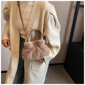 Sac seau en peluche rose-brun clair avec bandoulière en cuir porté sur un cardigan blanc