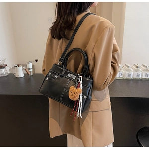 Detail of black faux leather handbag with contrast stitching and brown teddy bear charm