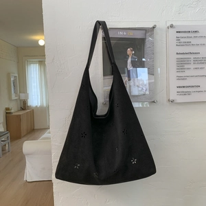 Detail of laser-cut floral patterns on a black suede tote bag hanging on a white wall