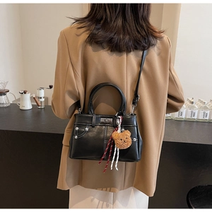 Detail of vintage black leather bag with white stitching and plush bear charm on model