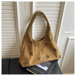 Détail du sac cabas en daim marron avec motifs floraux découpés au laser et un livre